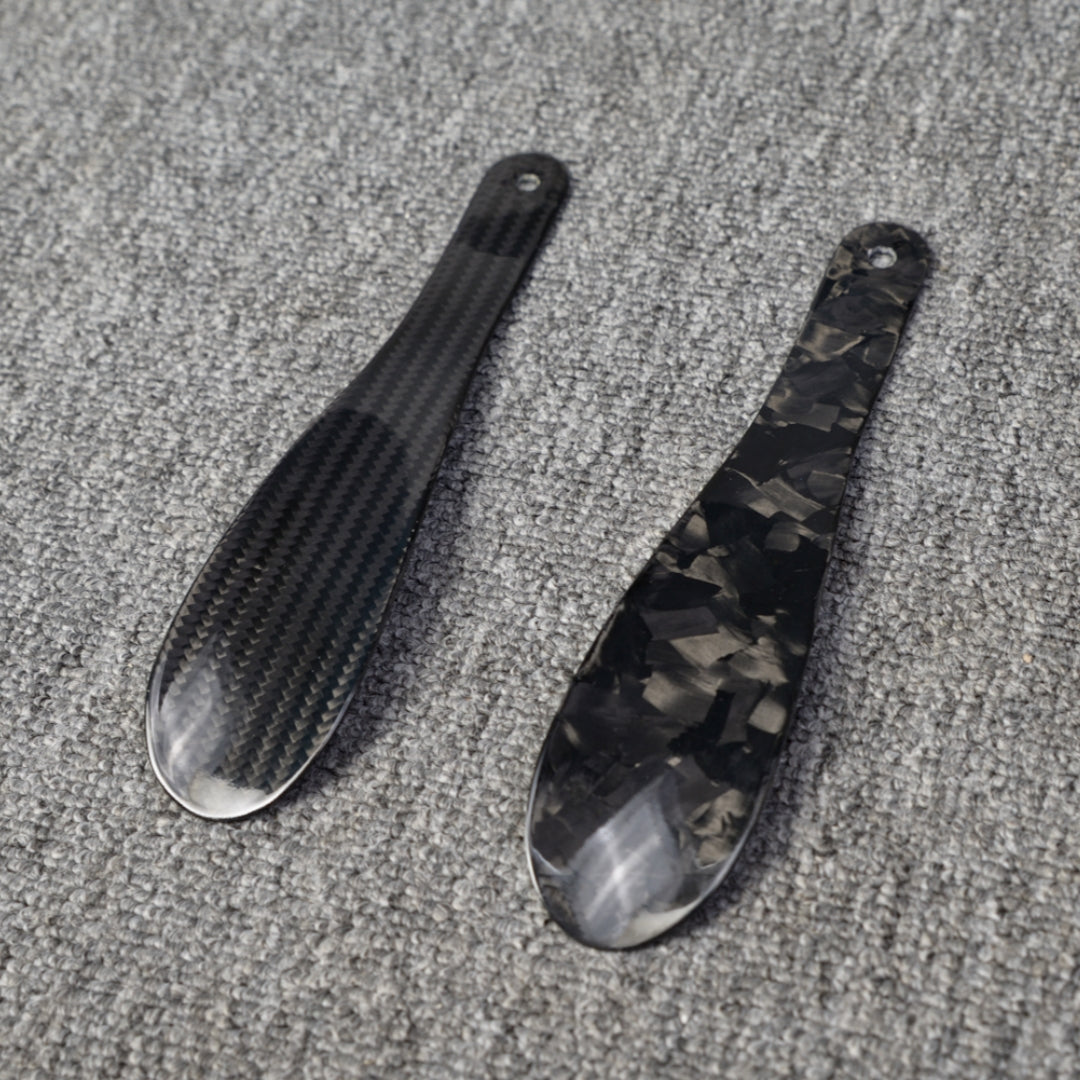 ### For “锻造碳纤维和4K碳纤维鞋扒子”：
Close-up detail of two carbon fiber shoe horns—one featuring a forged carbon texture and the other with a 4K carbon fiber woven pattern—placed on a gray textured surface.

### For “锻造碳纤维和3K碳纤维鞋扒子”：
Close-up detail of two carbon fiber shoe horns—one featuring a forged carbon texture and the other with a 3K carbon fiber woven pattern—displayed on a gray textured surface.