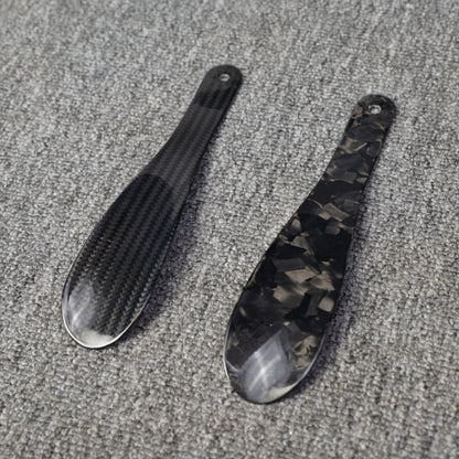 ### For “锻造碳纤维和4K碳纤维鞋扒子”：
Close-up detail of two carbon fiber shoe horns—one featuring a forged carbon texture and the other with a 4K carbon fiber woven pattern—placed on a gray textured surface.

### For “锻造碳纤维和3K碳纤维鞋扒子”：
Close-up detail of two carbon fiber shoe horns—one featuring a forged carbon texture and the other with a 3K carbon fiber woven pattern—displayed on a gray textured surface.