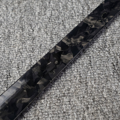 Close-up detail of a long forged carbon fiber shoe horn with a distinct chopped texture, placed on a gray textured fabric surface.