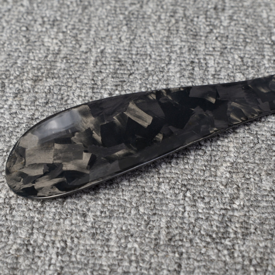 Close-up detail of a short forged carbon fiber shoe horn with a distinct chopped texture, placed on a gray textured surface.