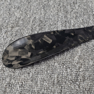 Close-up detail of a short forged carbon fiber shoe horn with a distinct chopped texture, placed on a gray textured surface.