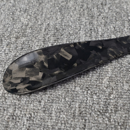 Close-up detail of a short forged carbon fiber shoe horn with a distinct chopped texture, placed on a gray textured surface.