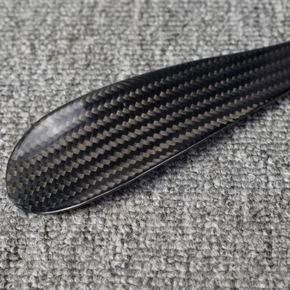 Close-up detail of a short 3K carbon fiber shoe horn with a distinct woven pattern, placed on a gray textured surface.