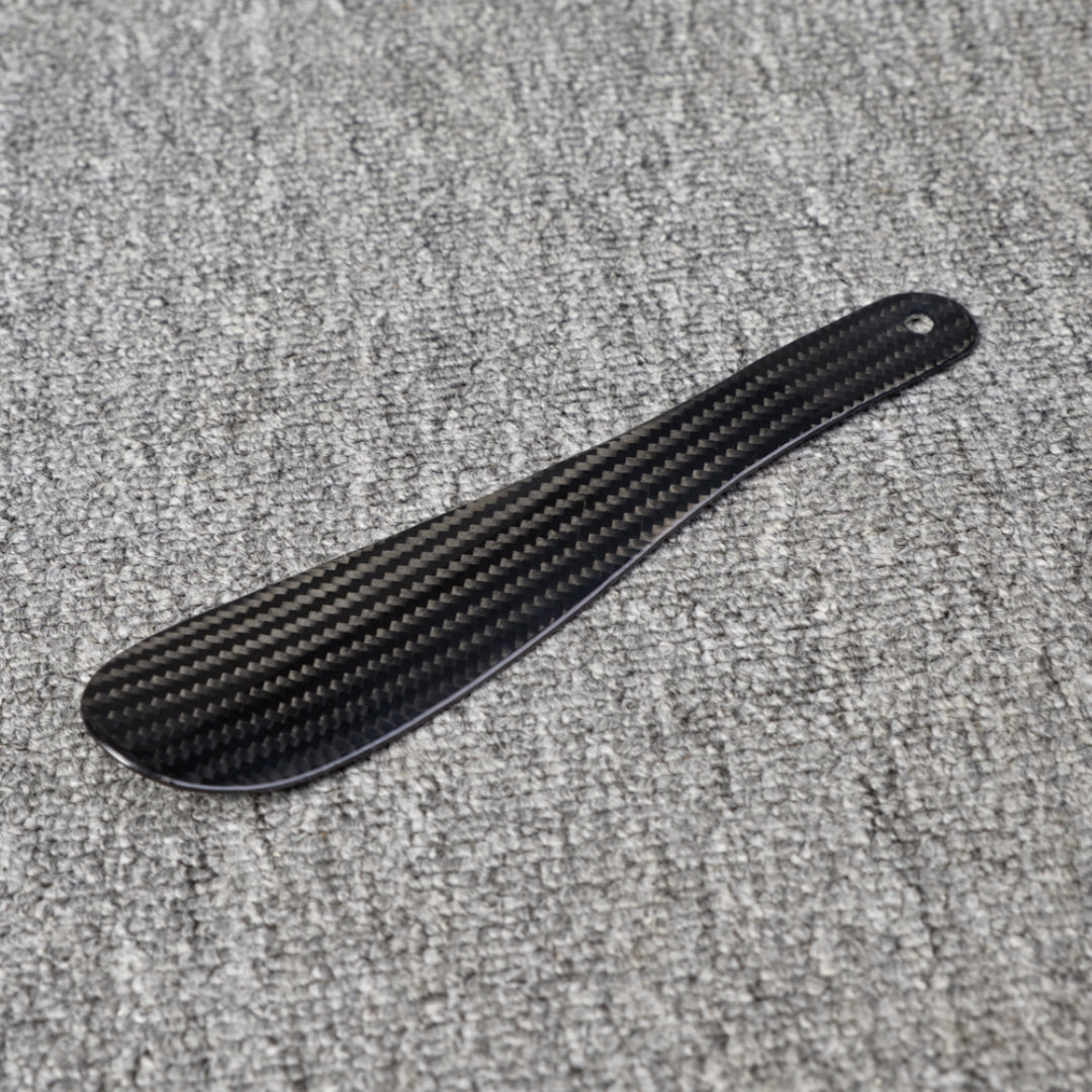 Close-up detail of a short 3K carbon fiber shoe horn with a distinct woven pattern, placed on a gray textured surface.