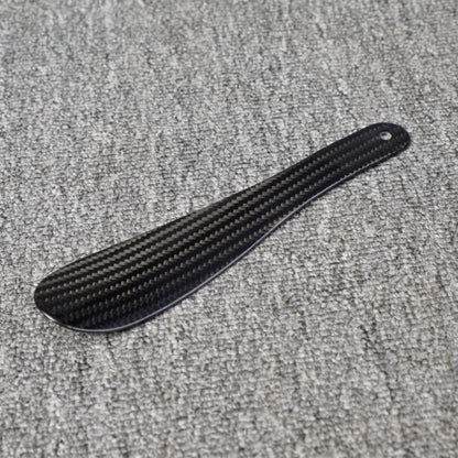 Close-up detail of a short 3K carbon fiber shoe horn with a distinct woven pattern, placed on a gray textured surface.