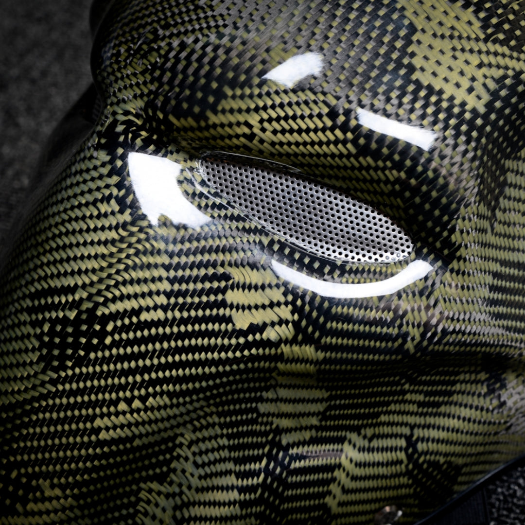 Close-up of a forged carbon fiber tactical mask with yellow and black pattern, featuring a mesh eye opening and glossy finish.