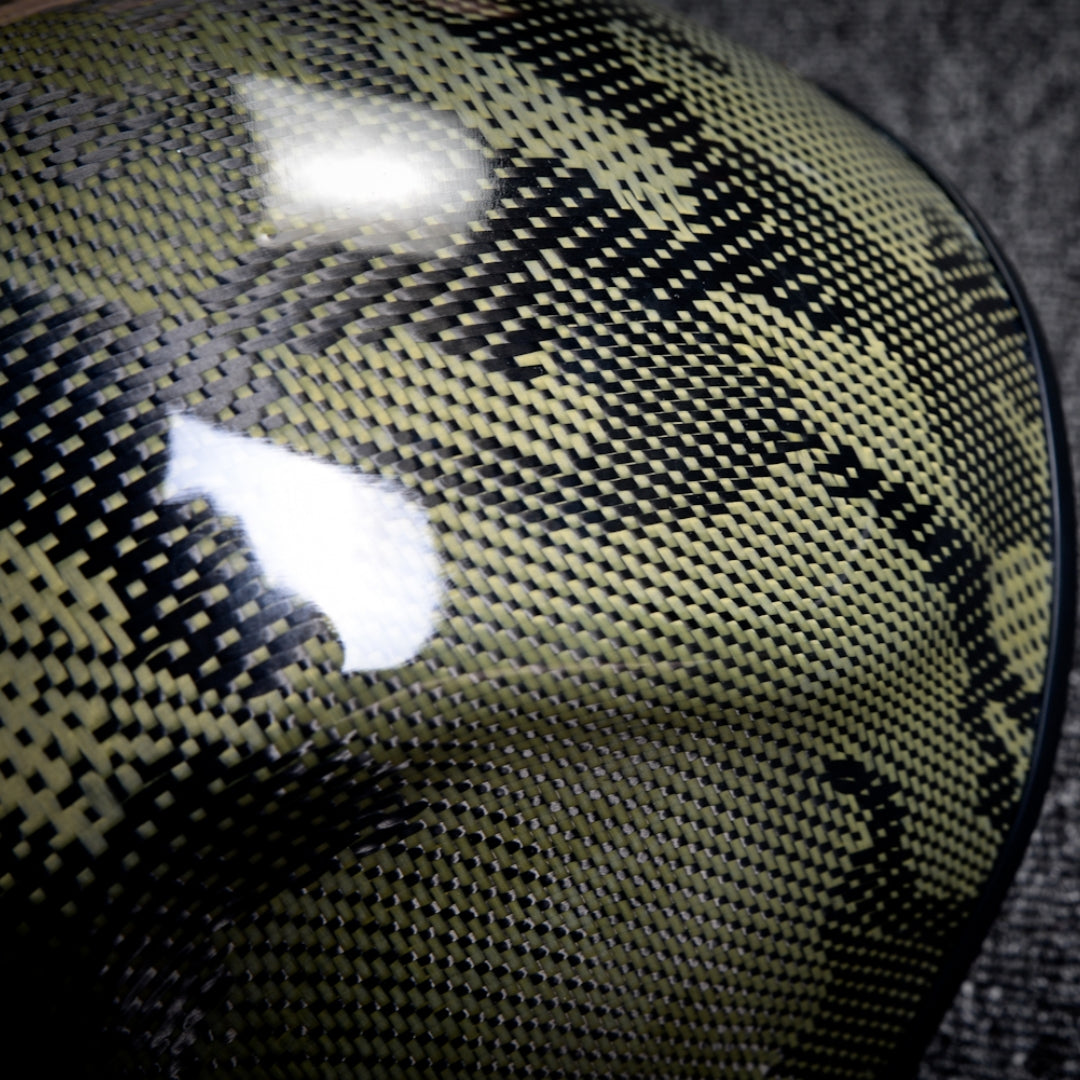 Close-up detail of a forged carbon fiber tactical mask featuring a yellow and black woven pattern with a glossy finish.