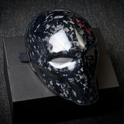 Close-up of a forged carbon fiber tactical mask with a speckled black-and-white pattern, mesh eye openings, and a glossy finish
