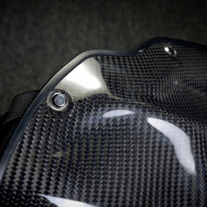 Close-up side detail of a black 3K twill carbon fiber tactical mask, showcasing the woven pattern, glossy finish, and metal rivet.