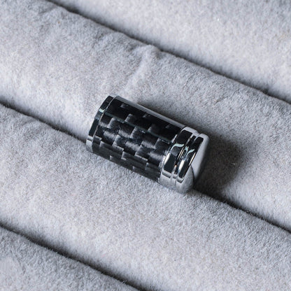 Close-up of a carbon fiber car tire valve stem cap with chrome detailing, placed on a light gray velvety surface.