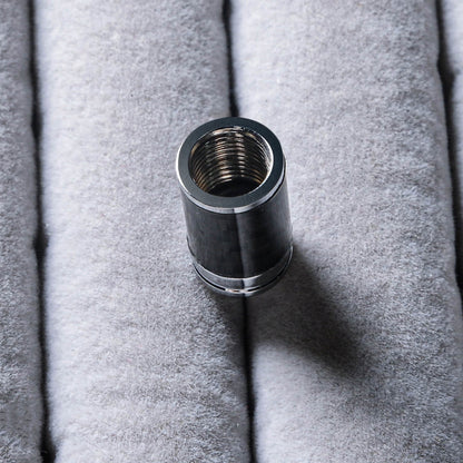 Close-up of a single carbon fiber car tire valve stem cap with metallic detailing, highlighting the threaded interior, resting on a soft gray textured surface.