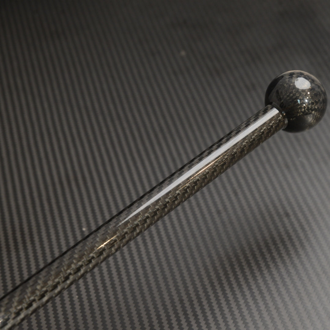 Close-up detail of a carbon fiber walking stick with a spherical top, showcasing the carbon fiber weave pattern, placed against a carbon fiber textured background.