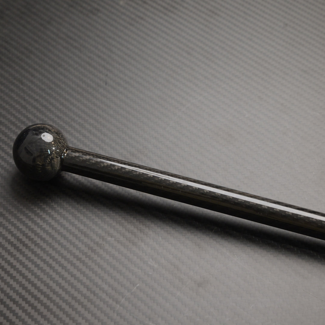 Close-up of a carbon fiber walking stick with a spherical top, showcasing the carbon fiber weave pattern, laid on a carbon fiber textured surface.
