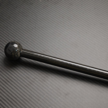 Close-up of a carbon fiber walking stick with a spherical top, showcasing the carbon fiber weave pattern, laid on a carbon fiber textured surface.