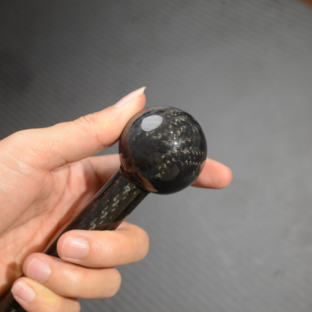 Close-up of a hand holding the spherical top of a carbon fiber cane, showcasing the carbon fiber weave pattern.