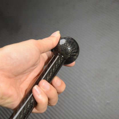 Close-up of a hand holding the spherical top of a carbon fiber cane, showcasing the carbon fiber weave pattern against a textured gray background.