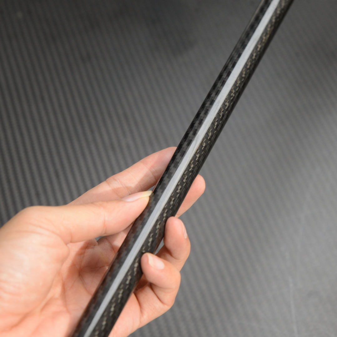 Close-up of a hand holding the shaft of a carbon fiber cane, showcasing the detailed carbon fiber weave pattern against a textured carbon fiber background.