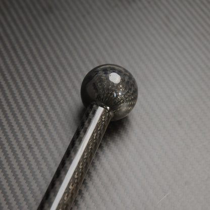 Close-up of the spherical top of a carbon fiber cane, showcasing the carbon fiber weave pattern, placed on a carbon fiber textured surface.