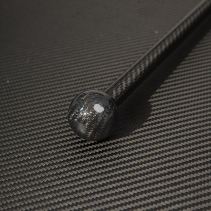 Close-up of the spherical top of a carbon fiber cane, showcasing the carbon fiber weave pattern, placed on a carbon fiber textured surface.