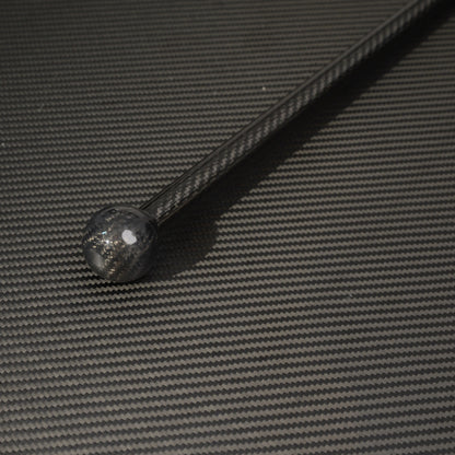 Close-up of a full-length carbon fiber cane with a spherical top, showcasing the carbon fiber weave pattern, placed on a carbon fiber textured surface.