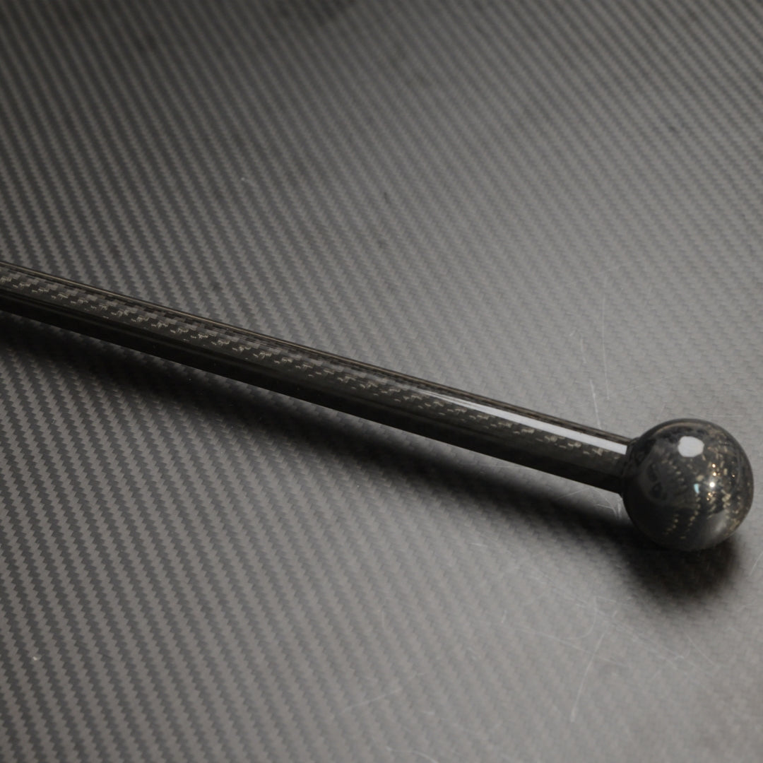 Close-up of a carbon fiber cane with a spherical top, showcasing the carbon fiber weave pattern, placed on a textured carbon fiber surface.