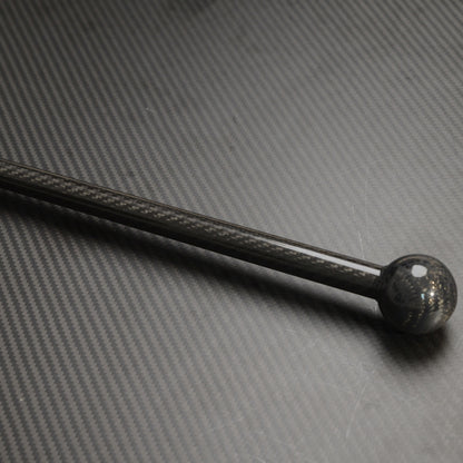 Close-up of a carbon fiber cane with a spherical top, showcasing the carbon fiber weave pattern, placed on a textured carbon fiber surface.