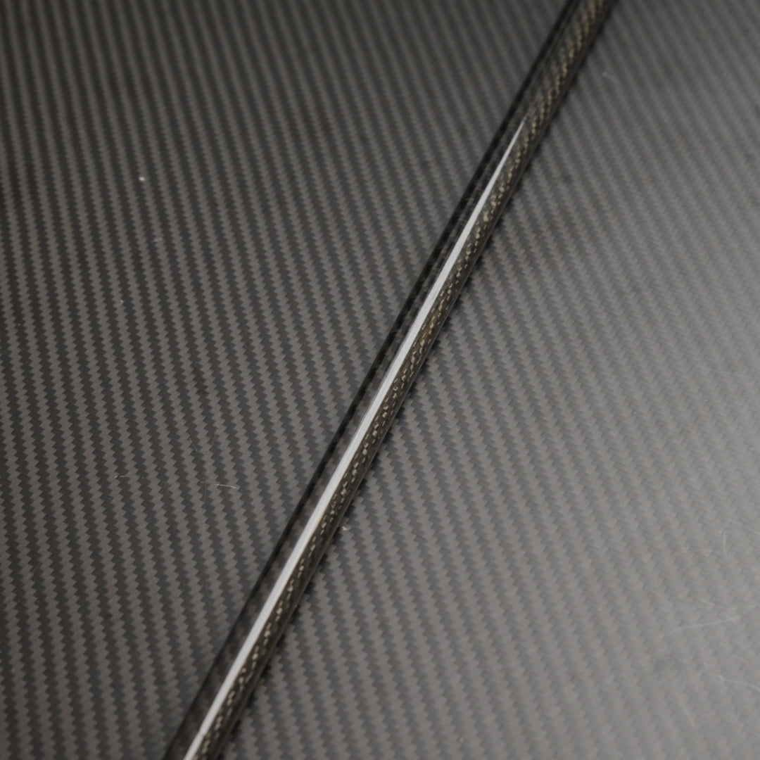 Close-up of a carbon fiber cane shaft, showcasing the detailed carbon fiber weave pattern, placed on a matching carbon fiber textured surface.