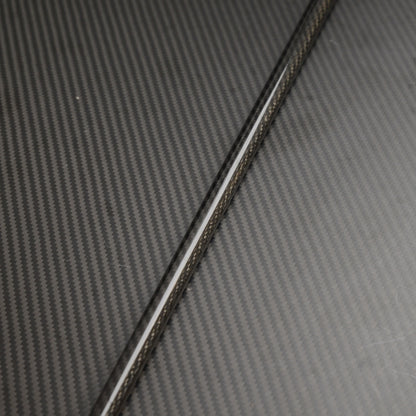 Close-up of a carbon fiber cane shaft, showcasing the detailed carbon fiber weave pattern, placed on a matching carbon fiber textured surface.