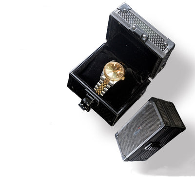 A close-up reveals an open 3K carbon fiber watch box, its lid adorned with a checkered pattern and lined with black velvet, displaying a gold wristwatch within.