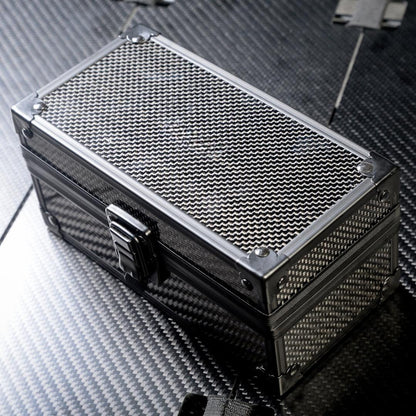 Close-up of a 3K carbon fiber watch box featuring a checkered pattern, metallic corner protectors, and a black latch, positioned on a carbon fiber textured surface.