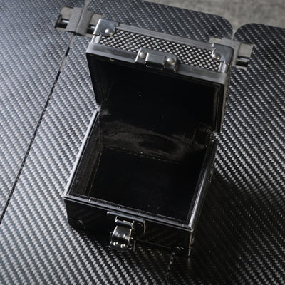 Close-up of an open 3K carbon fiber watch box with a black velvet interior, metallic latches, and a carbon fiber textured exterior