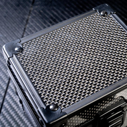Close-up top view of a 3K carbon fiber watch box featuring a checkered pattern and metallic corner reinforcements, placed on a carbon fiber textured surface.