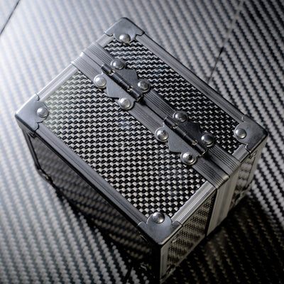 Close-up back view of a 3K carbon fiber watch box with a checkered pattern, metallic hinges adorned with rivets, and reinforced corners
