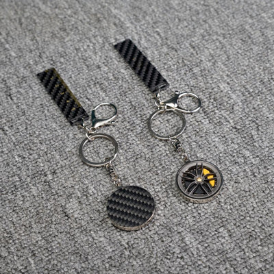 Close-up of two carbon fiber keychains-one featuring a wheel rim design with yellow brake calipers