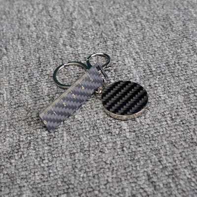 Close-up of a carbon fiber keychain featuring a ruler-shaped accent with measurement markings and a circular carbon fiber charm