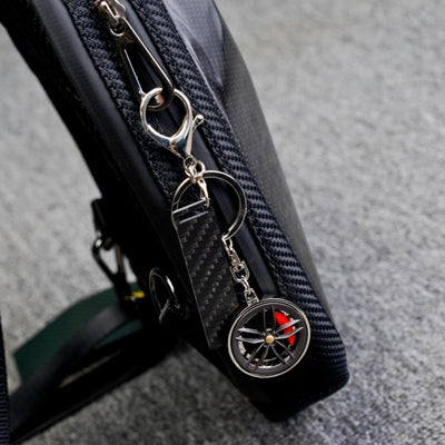 Close-up of a carbon fiber keychain with a wheel rim charm featuring red brake calipers and a carbon fiber-textured accent strip