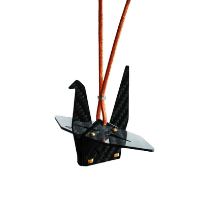 Black carbon fiber-textured origami crane pendant (ornament) with small gold-colored rivet details, suspended from an orange cord