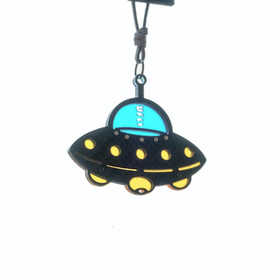 UFO-shaped accessory with a black carbon fiber-textured body. It has a bright turquoise cockpit section (printing "UFO" inside)
