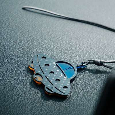 and small metallic rivets. The piece is attached to a gray leather cord (with metal hardware) and rests on a textured gray leather surface