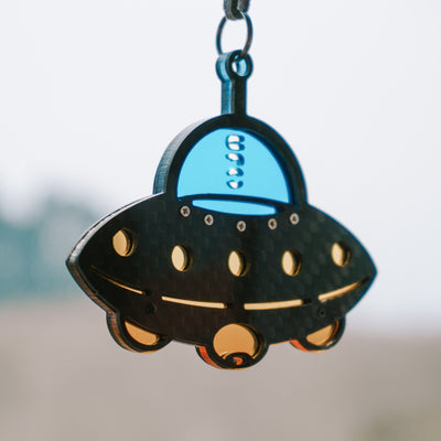 UFO-shaped hanging accessory with a black carbon fiber-textured body: It features a glossy bright blue cockpit section (printed with "UFO")