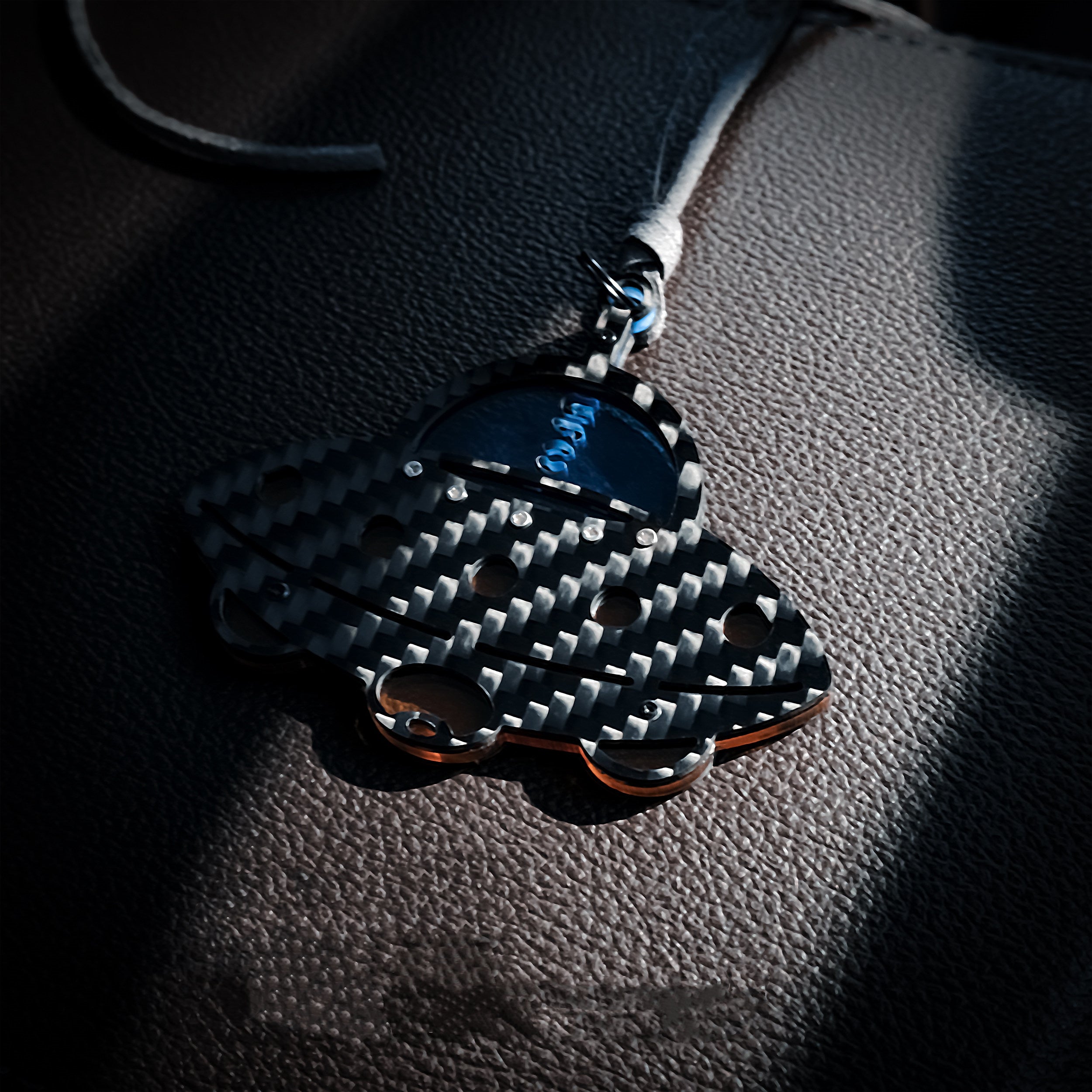 UFO-shaped car charm featuring a bold black-and-white carbon fiber weave texture: It has a glossy dark blue cockpit section (printed with "UFO")